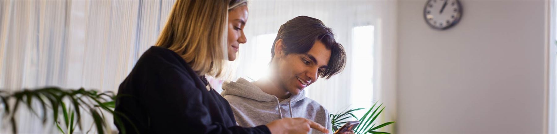 Två unga som sitter och surfar på deras mobiltelefoner. 