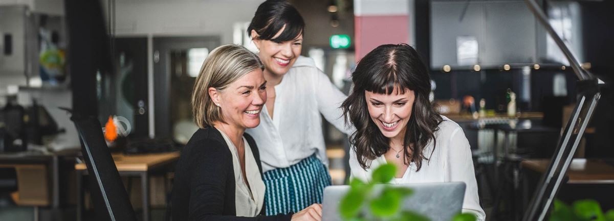 Three women discussing while watching laptop screen.